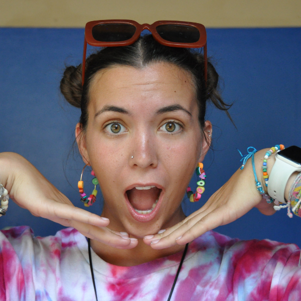 Girl Scout camp counselor with sunglasses on forehead, many bracelets on both wrists, hoop earrings, and posing with a shocked face with hands framing face